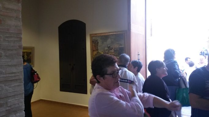 Mujer con gafas en primer plano, rodeada de un grupo de personas en un museo.